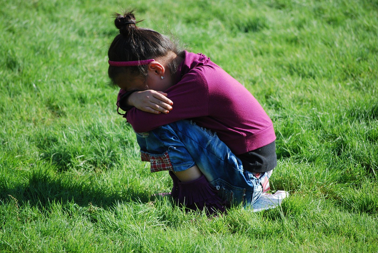 A young girl sitting curled up on the grass