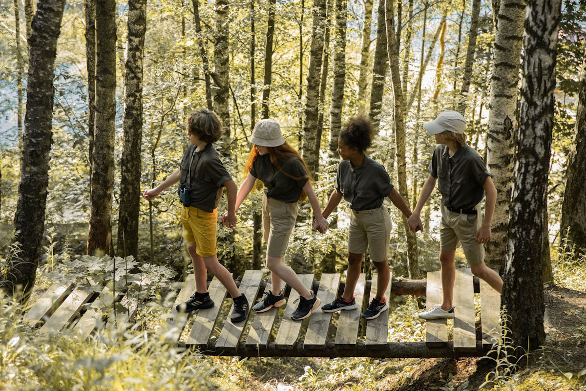 teenagers holding hands while walking on a wooden bridge in a forest