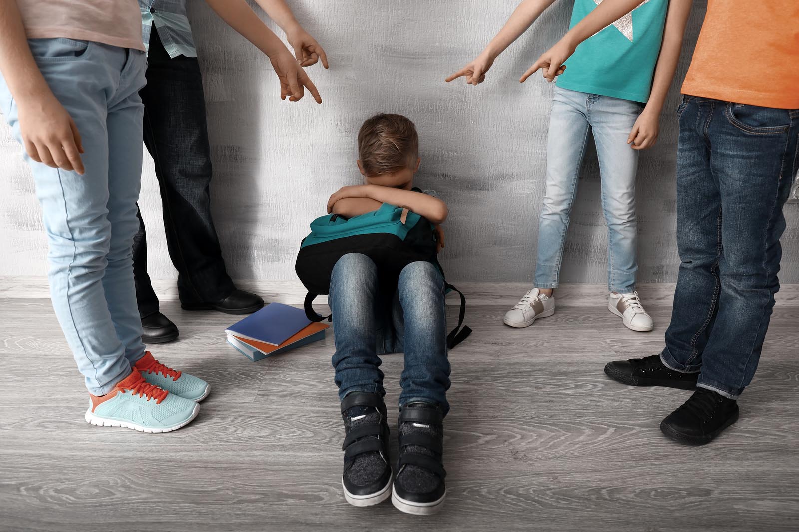 A group of students harassing a sad boy sitting on the floor