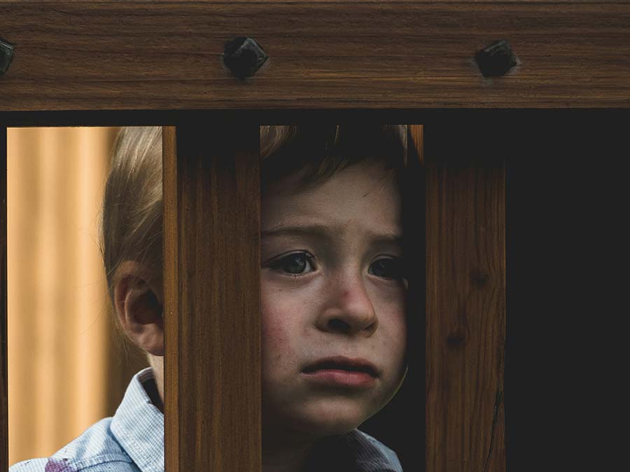 a sad-looking child looking through wooden railings