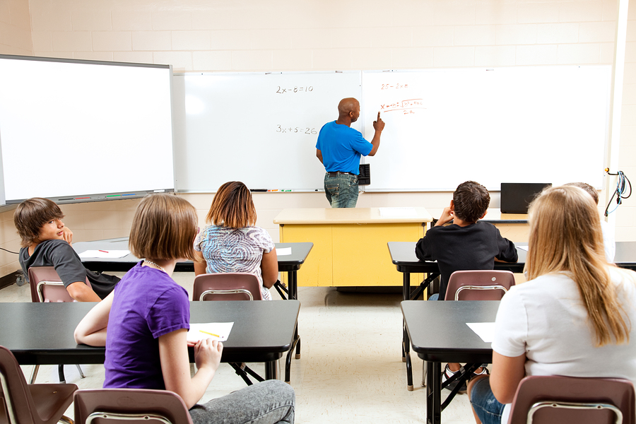 African-American male teacher writing on the whiteboard while teaching a group of students in a classroom