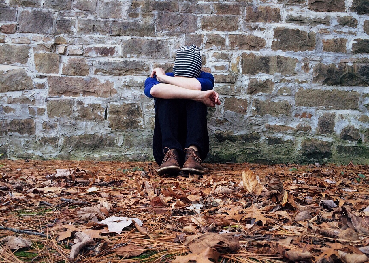 A sad student sitting curled up on the ground while leaning against a wall
