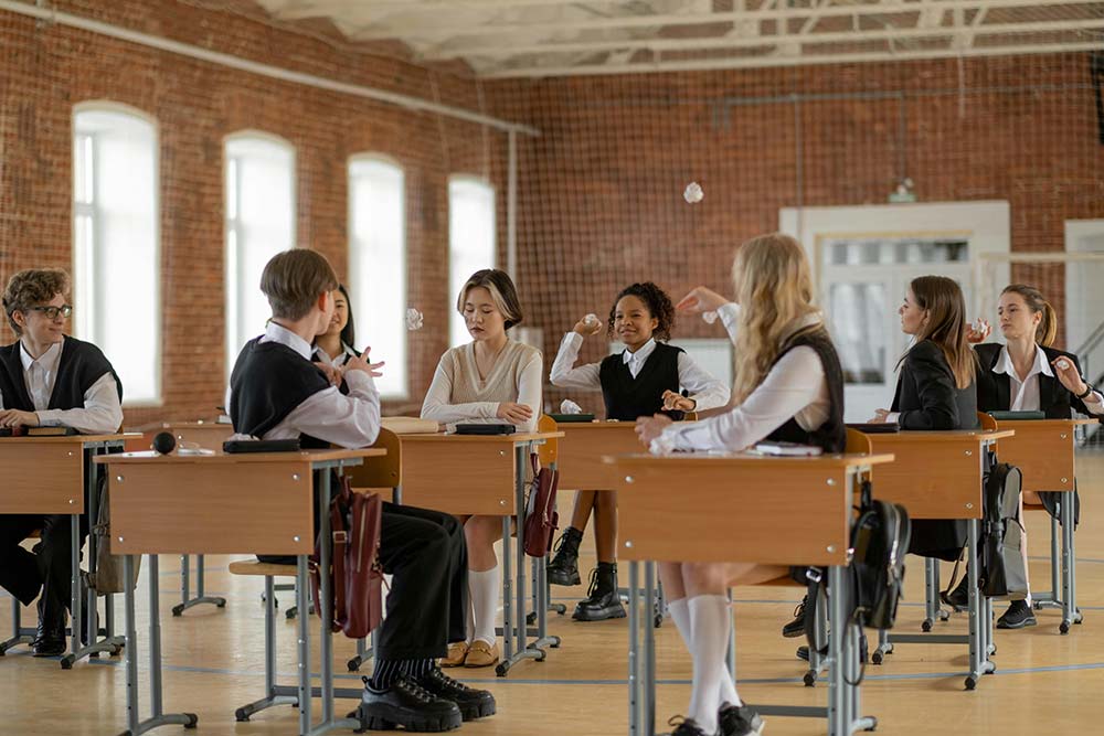 students in a classroom throwing crumpled-up papers at another studen